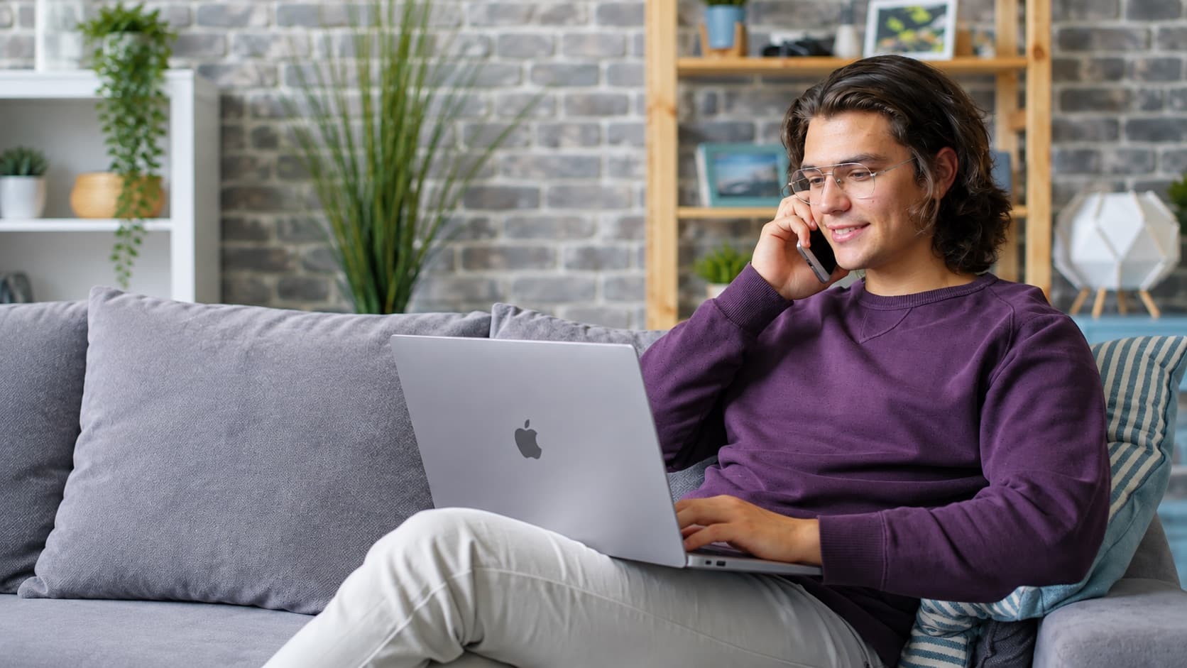 Person i soffan med laptop i knät, mitt i ett telefonsamtal